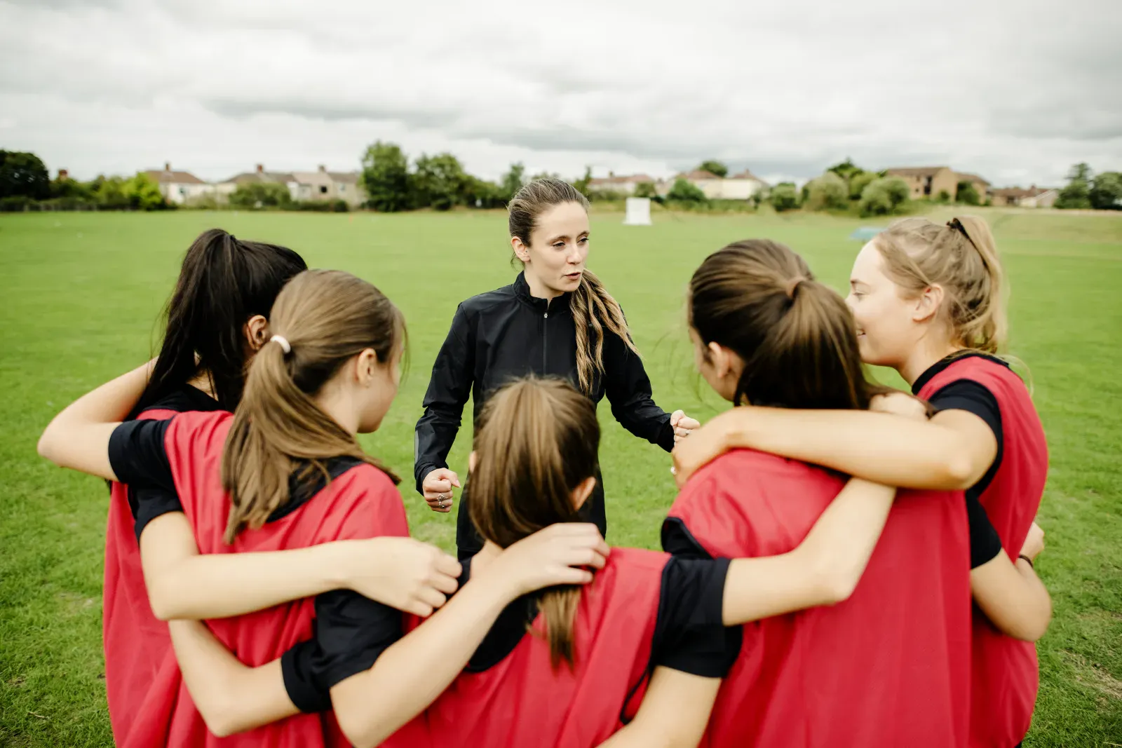 Équipe de football amateur réunie en cercle avec sa coach avant un match, en maillots personnalisés